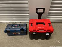 Photo showing a red and black rolling tool chest with telescoping handle and a blue plastic tool box on a concrete floor.