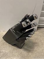 Side angle showing black knife block and stainless steel topped black handles of knives, blades inside block.