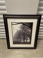 Full view of large framed art piece with foggy tree lined scene and bare trees.