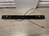 Full view of the black LG soundbar laid on a concrete floor, showing length and power cord.