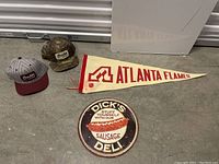 Vintage Atlanta Flames NHL pennant flag, two Brixton caps, and a round Dick's Deli metal sign on concrete floor.