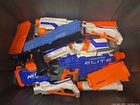 Photo showing multiple Nerf Elite blasters packed together in a bin, including blue, white, and orange colors.