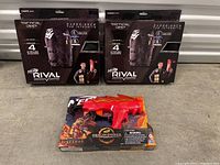 Photo showing two Nerf Rival Tactical Vests in packaging and one Nerf DragonPower Fireshot Blaster in original packaging on a shelf.