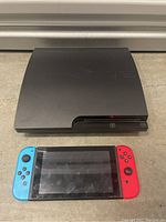 Front view of black Sony PlayStation 3 Slim console and front view of Nintendo Switch with Neon Blue and Neon Red Joy-Con attached.