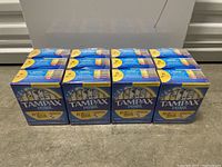 Four sealed boxes of Tampax Pearl tampons stacked in a row on a concrete floor against a white background.