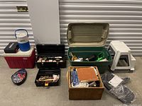 Overview photo showing multiple items including coolers, toolboxes, storage containers, step stools, and a plastic case with cables