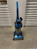 Full front view of blue upright vacuum cleaner with hose and clear dust container, showing handle and base.