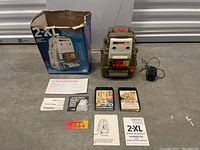 Wide shot showing robot, box, cables, manuals, cartridges and answer card on concrete floor.