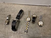 Five assorted wristwatches laid out on a carpeted floor, showing band and watch face details.