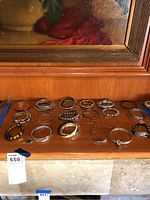 Photo of 19 assorted costume jewelry bracelets on a wooden surface showing a variety of bangle, chain, and beaded styles in metallic tones and colors.
