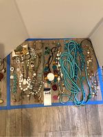 Top-down view of costume jewelry with multiple necklaces and bracelets laid out on the floor.