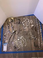 Overview shot of costume jewelry necklaces and bracelet laid out on floor, showing variety of pieces including chunky bead necklaces, chain links and pendants.
