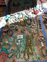 Top view of assorted turquoise, green, and coral costume jewelry including necklaces, bracelets, rings, and earrings laid out on a table.