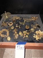 Photo showing full assortment of costume jewelry items including bracelets, pendants, charm necklaces arranged on a black cloth.