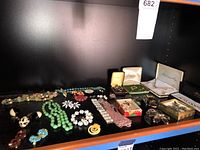 Full display of assorted costume jewelry including necklaces, earrings, pins, and jewelry boxes arranged on a shelf.