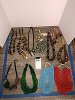 Full view of the 13 assorted costume jewelry necklaces laid flat including various bead and pendant styles in earth and bright tones.
