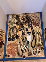Full view of the costume jewelry lot showing a variety of necklaces, earrings, and a pendant watch on chain. Includes beads in pink, purple, green, white, black, and orange tones.