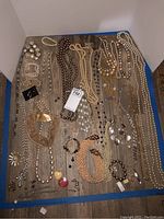 Overview of entire costume jewelry lot showing multiple pendants, necklaces, bracelets, and earrings scattered on floor against corner walls.