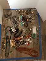Overview of costume jewelry lot on gray wood surface showing mix of necklaces, bracelets, earrings with different colors and styles.