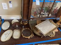 View of multiple vintage mirrored vanity trays arranged on the floor beneath a display cabinet, showing variety in shapes and frame styles.