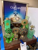 Front view of six decorative perfume bottles on wooden surface with Guerlain poster backdrop