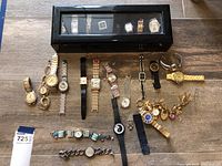 Overview of 11 watches outside the black storage box laid out on a wooden surface, showing variety in styles and bands