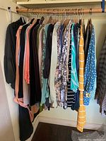 Photo of women's clothing items hanging on a rack showing a variety of tops and sweaters in different colors and styles.
