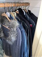 Side view of gray sweater with thick fur collar and denim and leather jackets on hangers