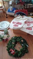 Christmas wreath with assorted decorations on floor along with two 'Reindeer Feed' gift bags and decorative pine centerpiece.