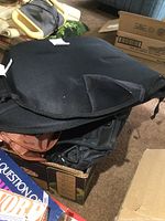 Photo of the black heated seat cushion showing padding and contour folds, placed over a cardboard box with other items partially visible.