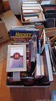 Top view of box full of hockey books and DVDs showing titles 'Hockey: Road to the Championship' and 'Hockey A People's History'