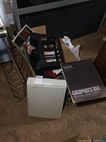 Umax flatbed scanner visible with wear and scuffs, black metal magazine rack behind it, and Bee Graphics 360 layout paper on carpet