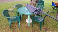 Overall view of green outdoor resin patio table with three chairs, reclining chair, umbrella laid on top, and stand on grass