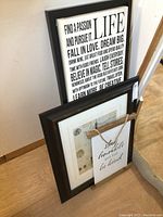 Three wall art pieces including a large framed inspirational quote, a framed vintage style print with a smaller hanging metal sign having a wood frame and rope.