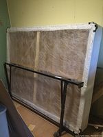 Metal adjustable bed frame positioned leaning against queen box spring in a room with wood flooring and a green wall.