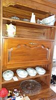 Top shelf with two salt and pepper shaker sets, nesting teapot with cup and plate, four covered scallop dishes and one large round glass platter on bottom shelf.
