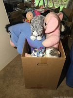 Box filled with various sized stuffed animals including a large blue donkey, a gray dog, a pink elephant, and other animals visible inside the box.