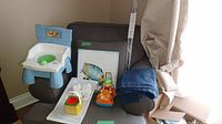 Photo of toddler potty chair, stacking cubes, toy car, art and blue curtains all on grey recliner chair.