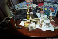 Photo of the entire lot showing the rock tumbler kit, wire dish rack, various bottles, jars, brushes, doll, and Sudoku game positioned on a table surface.