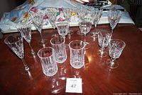 Top-down view of 12 pieces of clear cut crystal glassware arranged on a wooden table including 6 wine glasses, 3 tumblers, and 3 smaller stemmed glasses.