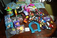Overview of assorted kids toys on a table, showing multiple small vehicles, sealed Polly Pocket accessory bags, and plastic animal toys spread out