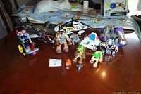 Multiple Rescue Hero toys including figures and small accessories along with two vehicles - a Tonka helicopter and stealth jet on a table.
