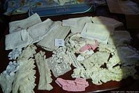 Overview of lace doilies, lace edge trimmings including white, cream, and some pink pieces spread out on a table.