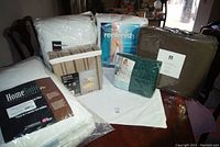 All items arranged on a table showing pillows, mattress pads, bedding sheets, blanket, and sofa cover in original packaging.
