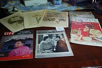 Photo of various vintage magazines and posters on a table including Pictorial Review issues from mid-1930s, Life 1955, Royal Romance 1960, among others