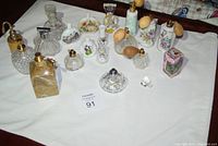 Full view of all perfume bottles and misters on white cloth, displaying variety in size, shape, and material.
