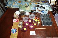 Photo of lot items on a table including pug pillow, candles, glass dishes, crib board, digital camera, exercise ball box, mini rake, and plastic holders.