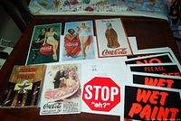 Photo of Coca-Cola reproduction tin plaques, plastic signs, and a book on totem poles arranged on a table.