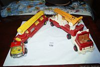 Three vintage fire trucks laid on white paper on a table including two Tonka trucks and one Fisher Price truck.