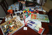 Full lot overview showing toys arranged on a table including wooden xylophone, doll stands, various toy cars, animal figures, board game, and Darth Vader doll.